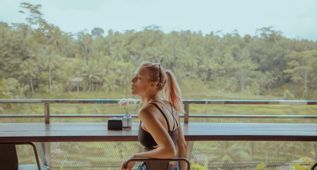 A woman sitting at an outdoor table with a view of lush greenery.