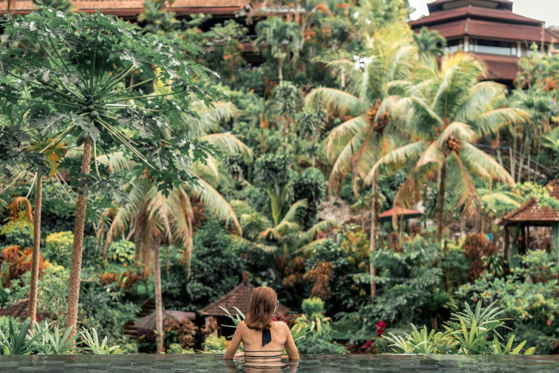 A woman sitting in an infinity pool, surrounded by lush tropical vegetation.