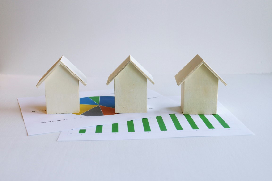 Three small wooden house models placed on top of pie and bar charts.