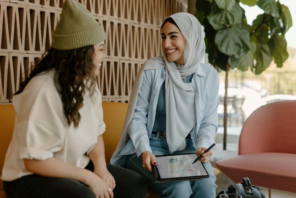 Two women sitting together, smiling, one with a tablet.