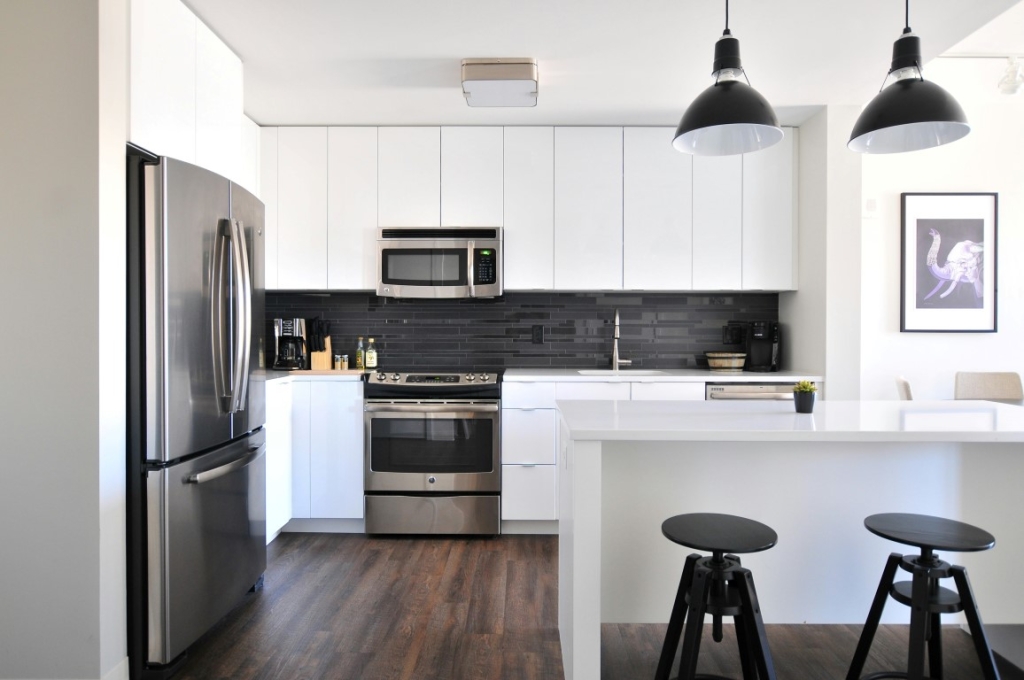 A modern kitchen with white cabinets, a stainless steel refrigerator, and two black pendant lights.