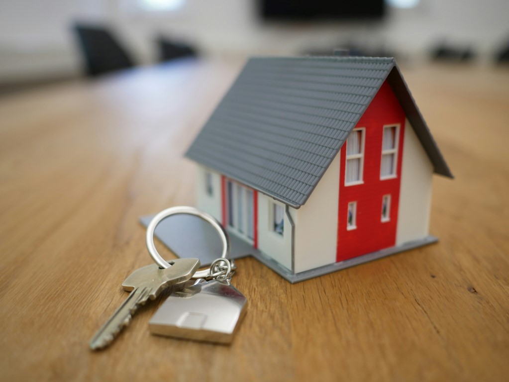 A small model house with keys on a wooden surface.