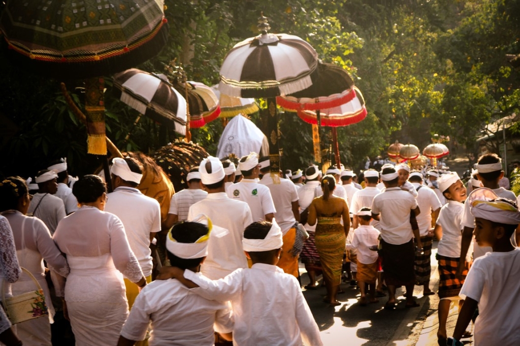 A procession of people dressed in white, carrying umbrellas during a traditional ceremony.